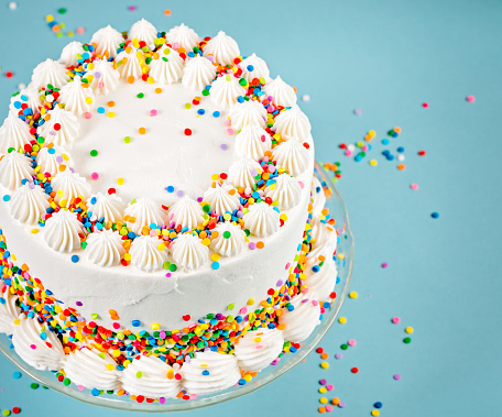 White Birthday cake with colorful Sprinkles over a blue background.
