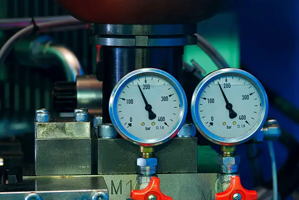 Two pressure gauge with arrows indicating pressure of oil in bar. Pipes and wires out of focus.