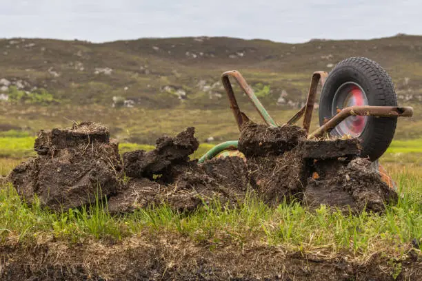 Inverasdale, Scotland - June 9, 2012: Closeup of turned over rusty wheel barrel at peat digging site. Green grass as background.