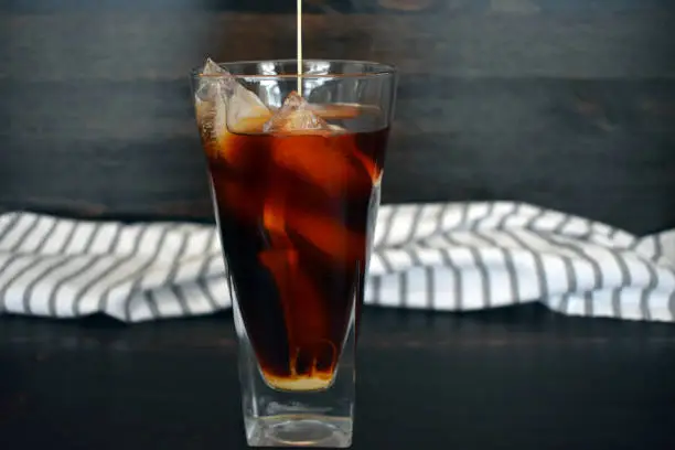 A tall glass of iced coffee with a cloth napkin in the background