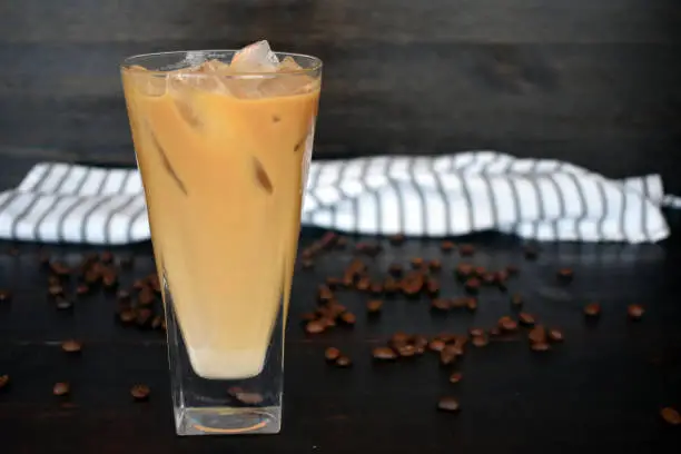 A tall glass of iced coffee with a cloth napkin and coffee beans in the background