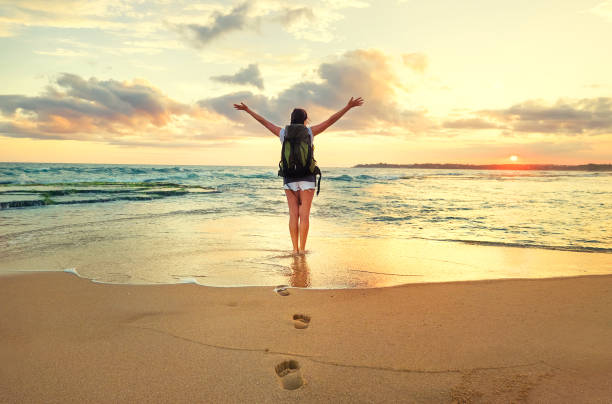 istock Woman backpacker stay on ocean surf line at sunset time 932050646