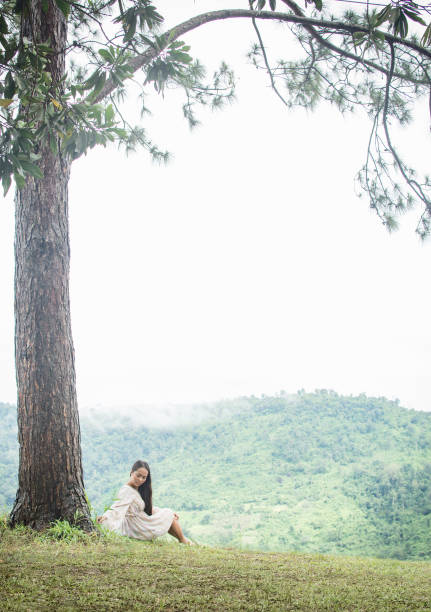 istock Beautiful Asian woman sitting beside tall tree on mountain with clouds. 932071074