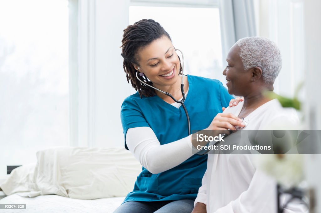 Female nurse checks patient's vital signs Young African American home healthcare nurse checks a senior female patient's vital signs. The senior woman is recovering at home from a recent surgery. Doctor Stock Photo