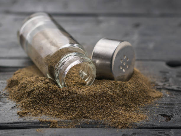 istock Black pepper is poured from a glass pepper jar on a wooden table. 932079116