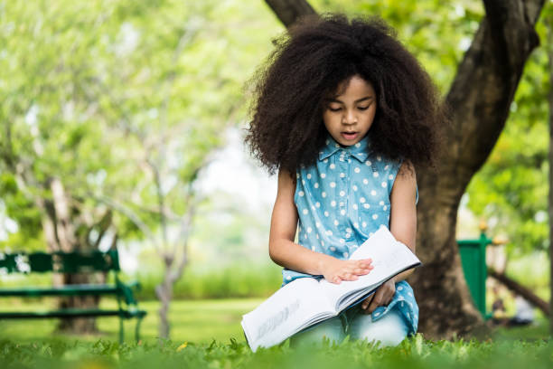 istock Beautiful girl reading a book while sitting on green grass in a park 932081680