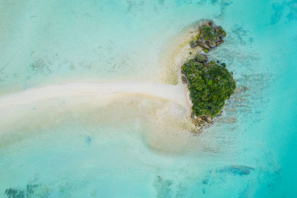 Komodo National Park Small Paradise Beach Atoll Islet. Drone view towards a small paradise Atoll Islet surrounded with coral reef under blue summer sky in the Komodo National Park. Tourist Tourboat cruising in the background along the island. Komodo National Park, Flores Sea, Labuan Bajo, East Nusa Tenggara - Flores, Indonesia, Southeast-Asia.