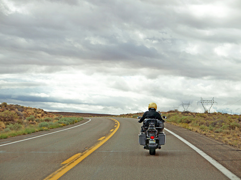 Lonely road with biker travelling through the Arizona desert landscape, dramatic sky ahead