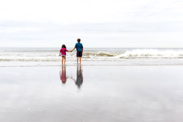 istock Brother and sister standing hand on the beach 932093322