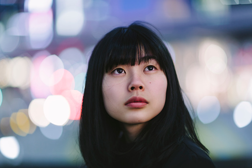 A portrait of a young Japanese woman in the city at night.