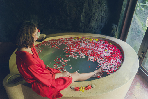 Young Caucasian woman  taking hot tub with flower petals