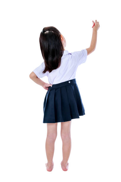 Full body. Back view of young preschool child in uniform standing akimbo. Asian girl writing with red crayon. Education and people concept. Isolated on white background. Great for your design or text.