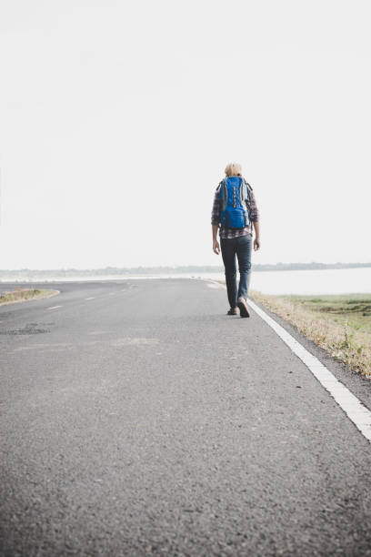 istock Young tourist man walking on a countryside road. 932109006