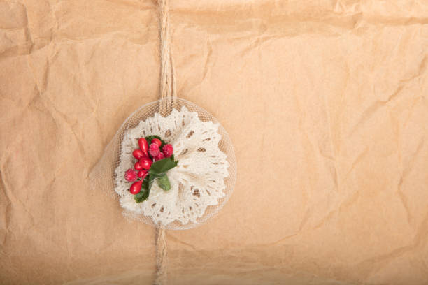 Close up view of a gift in crumpled vintage brown recycle paper tied with string and attached decoration with red berries on a white background