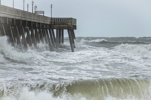 An incoming storm causes massive surf and storm surge to crash into a concrete beach pier.