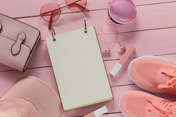 istock spring flat lay in rose tone. empty notebook with pink sneakers, baseball cap, pink sunglasses, pink lip gloss, pink headphones on a pink wooden plank background. 932140816