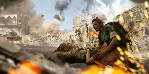 A female soldier medic wearing combat military uniform and backpack kneels on the ground and shouts for help whilst holding the head of an injured female colleague on her lap. The military personnel are both in a the middle of war zone amidst ruined buildings near explosions, smoke and fire.