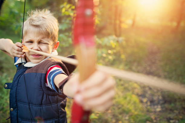 Little boy shooting bow in forest Little boy aged 8 playing ranger in forest. The boy is shooting a bow at imaginary beasts in forest. archery bow stock pictures, royalty-free photos & images