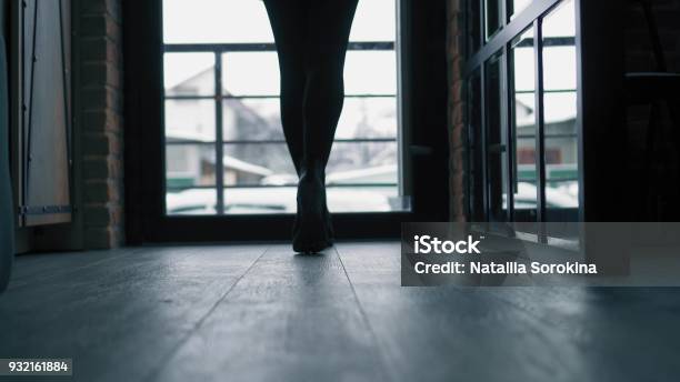 Woman In Black Boots Walking Along Dark Hallway From Camera To Door And Back Stock Photo - Download Image Now