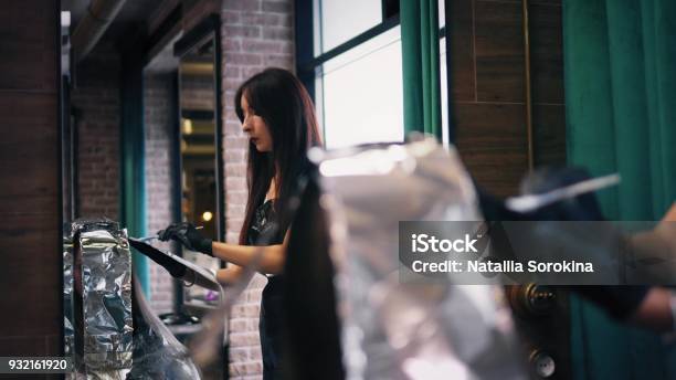 Hairdresser Is Applying Hair Dye And Foil On Womans Long Hair In Front Of The Mirror Back View Stock Photo - Download Image Now