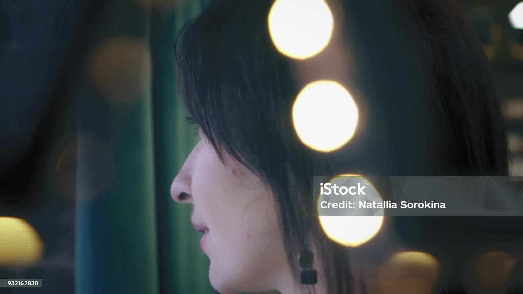Beautiful brunette is looking out the window, with green background. Closeup, profile. Portrait. Twinkle lights Beautiful brunette is looking out the window, with green background. Closeup, profile. Portrait. Twinkle lights. Adult Stock Photo