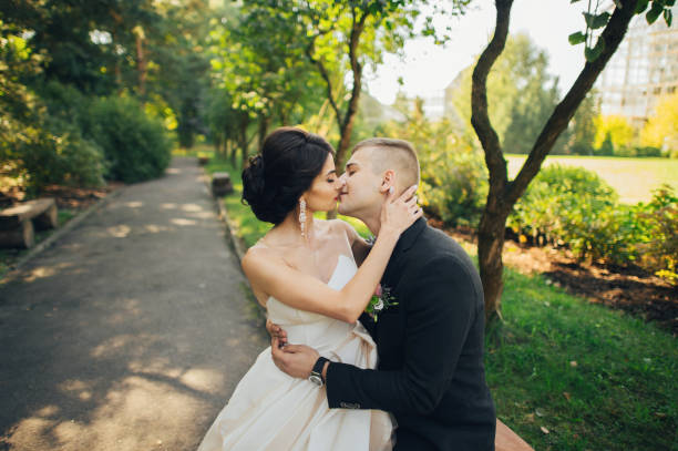 istock Confident elegant groom and beautiful shy bride holding hands outdoors closeup 932185818