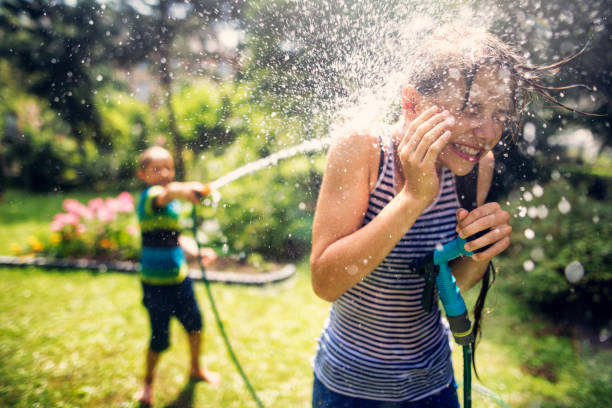 enfants ayant des éclaboussures fun dans back yard - spraying water photos et images de collection