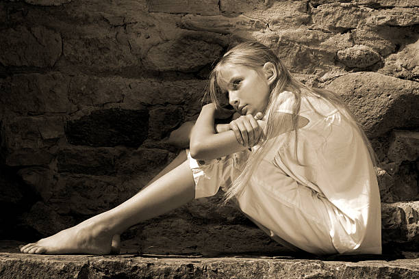Portrait of a pretty teen girl posing outside a wooden exterior with a daydream expression on her face. She has long brunette hair and she is wearing casual clothing. High resolution photograph processed in warm vintage sepia tones. Shot from the waist up. Vertical composition.