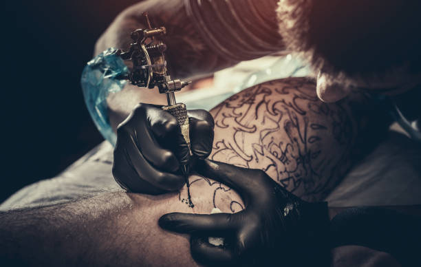 istock Tattoo master making tattoo on customer's leg 932193928