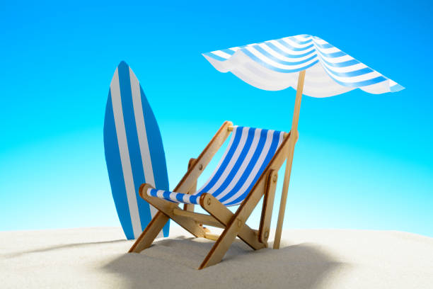 istock Deck chair under an umbrella and a surfboard on sandy beach 932206278