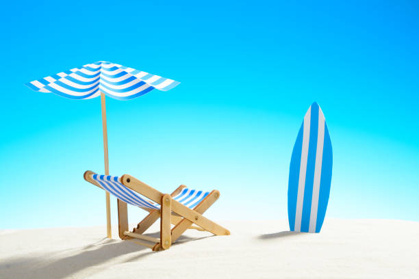 istock Deck chair under an umbrella and a surfboard on sandy beach 932206316