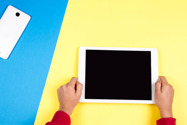 istock Kid hands holding tablet computer on blue and yellow background 932211934
