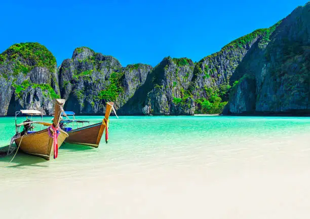 Famous scenic Maya Bay beach at Ko Phi Phi Leh Island with two traditional longtail taxi boats mooring and steep limestone hills in background, Thailand, part of Krabi Province, Andaman Sea