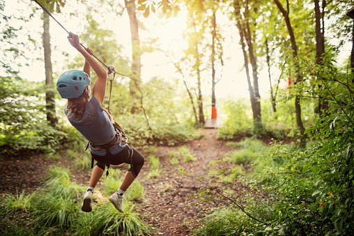 Teenage girl wearing a helmet zipping on a line in forest.\nNikon D810