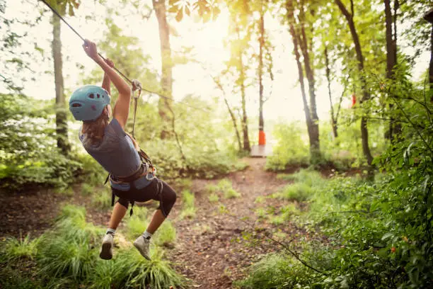 Teenage girl wearing a helmet zipping on a line in forest.
Nikon D810