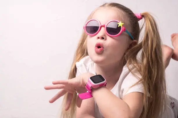 Photo of Technology for children: a girl wearing pink glasses uses a smartwatch.