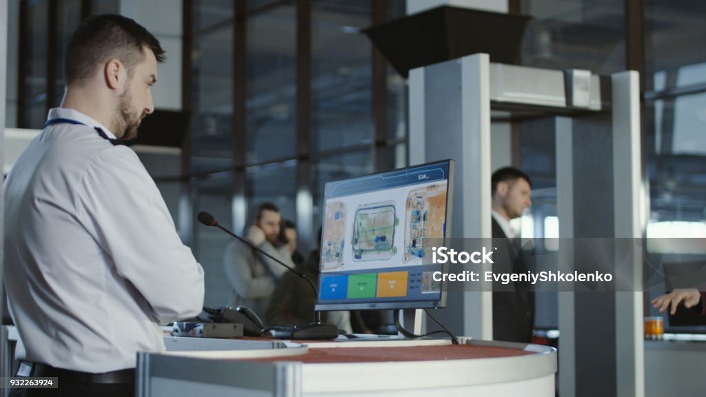 Airport worker exploring x-ray of baggage Man in uniform standing at counter at checking point and watching at monitor with x-ray of luggage. Airport Stock Photo