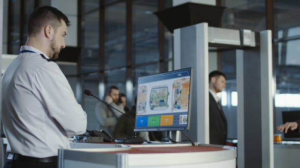 Airport worker exploring x-ray of baggage Man in uniform standing at counter at checking point and watching at monitor with x-ray of luggage. security staff photos stock pictures, royalty-free photos & images