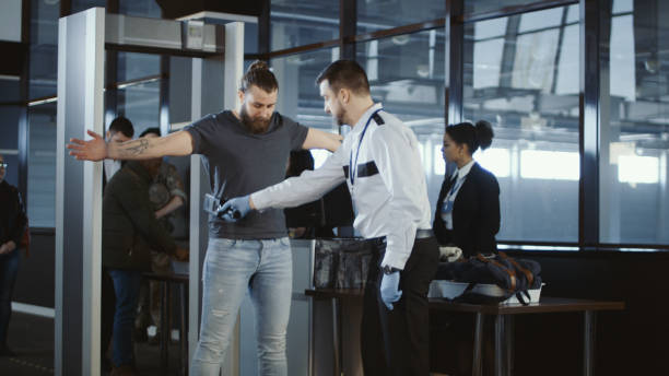 Security agent patting down a male passenger Security agent at an airport check-in gate patting down a bearded casual male passenger with outstretched arms after he passes through the metal detector scanner in the departures hall. customs official photos stock pictures, royalty-free photos & images