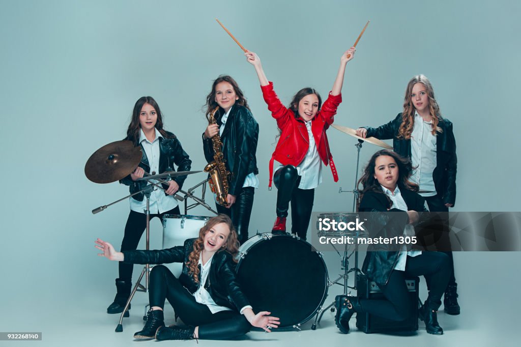 The teen music band performing in a recording studio Teen music band performing in a recording studio. The group of girls standing together and posing at camera. Studio portrait of young attractive fashion caucasian teen girls dressed inblack leather jackets grouped together. Kids fashion and rock concept Performance Group Stock Photo