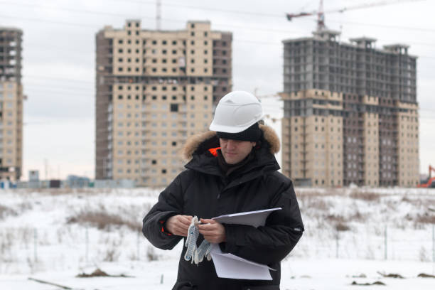 istock Worker or engineer holding drawing in hands and reading it on background of new apartment buildings and construction cranes on background. Architect engineer concept. Soft focus. 932270686