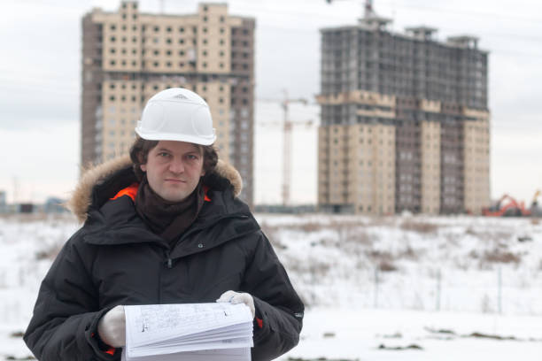 istock Worker or engineer holding drawing in hands and reading it on background of new apartment buildings and construction cranes on background. Architect engineer concept. Soft focus. 932270912
