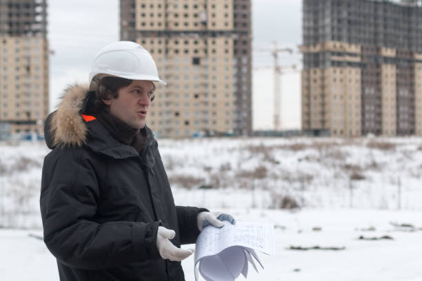 istock Worker or engineer holding drawing in hands and reading it on background of new apartment buildings and construction cranes on background. Architect engineer concept. Soft focus. 932270980