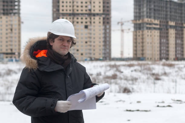 istock Worker or engineer holding drawing in hands and reading it on background of new apartment buildings and construction cranes on background. Architect engineer concept. Soft focus. 932271052