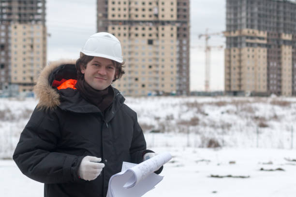 istock Worker or engineer holding drawing in hands and reading it on background of new apartment buildings and construction cranes on background. Architect engineer concept. Soft focus. 932271340