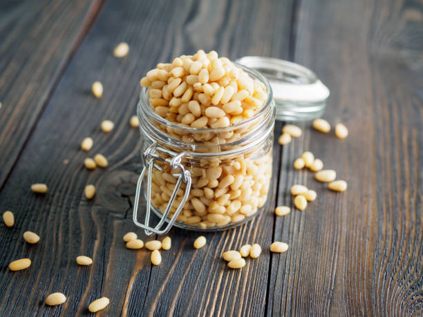 side view of glass jar with a handful of pine nut, cedar nuts on a wooden background, selective focus - pine nut nut seed vegan food imagens e fotografias de stock