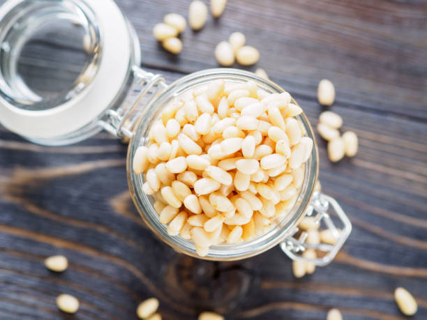 top view of glass jar with a handful of pine nut, cedar nuts on a wooden background, selective focus. - pine nut nut seed vegan food imagens e fotografias de stock