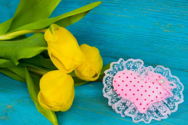 yellow tulips with pink textile heart on turquoise wooden table