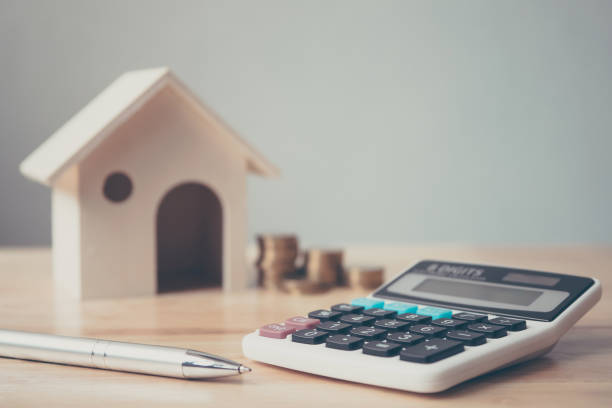 木造の家とコイン スタックと木製のテーブルの上にペン電卓。不動産投資、住宅抵当金融の概念 - 税金 ストックフォトと画像