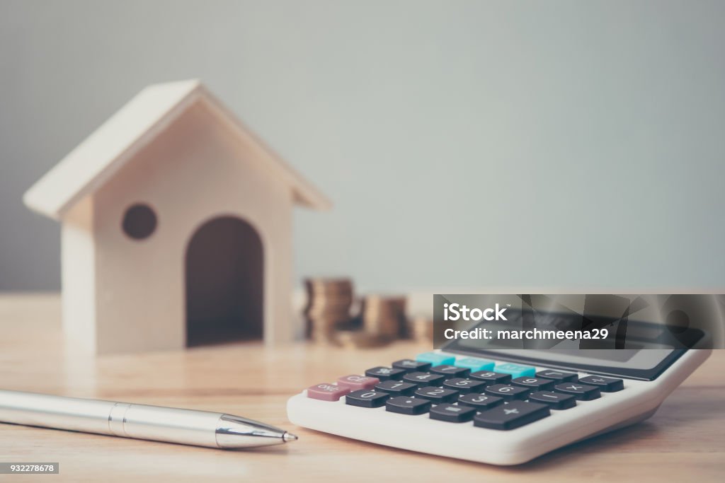 Calculadora com pilha de moedas e casa de madeira e caneta na mesa de madeira. Casa e propriedade de investimento financeiro conceito de hipoteca - Foto de stock de Casa royalty-free